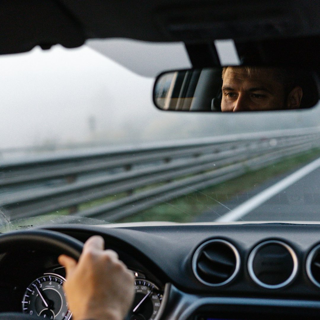 Chauffeur VTC-Haute-Savoie Conducteur regardant dans le rétroviseur sur une route brumeuse.