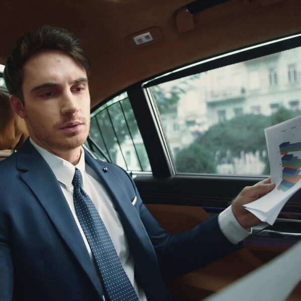 Passager Classe-Affaires VTC Homme en costume assis dans une voiture, tenant des documents colorés.
