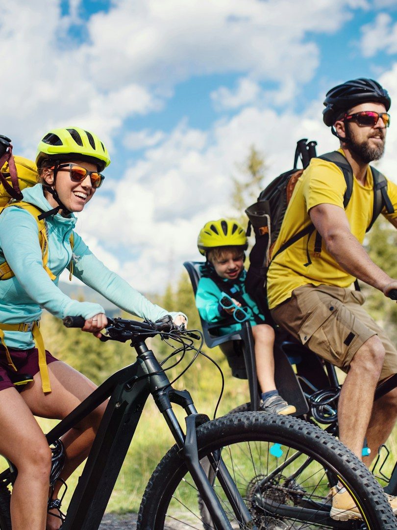 Portage Bagages randonnée à vélo avec VTC-Haute-Savoie Famille à vélo sur un sentier, enfants transportés dans des remorques. Ciel dégagé.